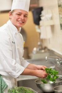 Culinary Immersion student in chef's whites sorts herbs into a colander